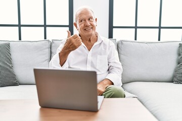 Sticker - Senior man using laptop at home sitting on the sofa smiling with happy face looking and pointing to the side with thumb up.