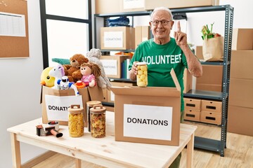 Poster - Senior man volunteer holding donations box putting food into a box surprised with an idea or question pointing finger with happy face, number one