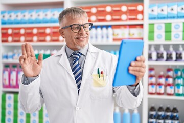 Sticker - Hispanic man with grey hair working at pharmacy drugstore doing video call with tablet looking positive and happy standing and smiling with a confident smile showing teeth