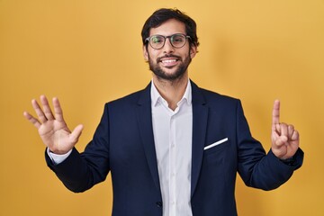 Sticker - Handsome latin man standing over yellow background showing and pointing up with fingers number six while smiling confident and happy.