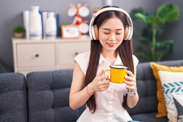 Wall Mural - Young chinese woman listening to music drinking coffee at home