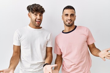 Wall Mural - Young gay couple standing over isolated background smiling cheerful with open arms as friendly welcome, positive and confident greetings