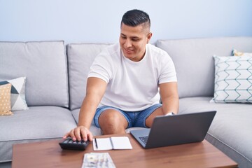 Wall Mural - Young latin man using laptop accounting at home