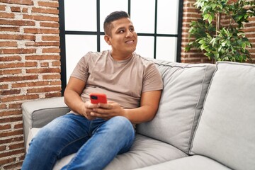 Canvas Print - Young latin man using smartphone sitting on sofa at home