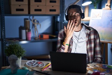 Poster - Young hispanic man sitting at art studio with laptop late at night bored yawning tired covering mouth with hand. restless and sleepiness.