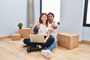 Poster - Young couple using laptop at new home smiling friendly offering handshake as greeting and welcoming. successful business.