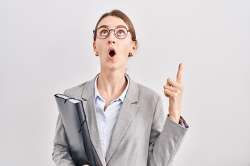 Canvas Print - Young caucasian woman wearing business clothes and glasses amazed and surprised looking up and pointing with fingers and raised arms.