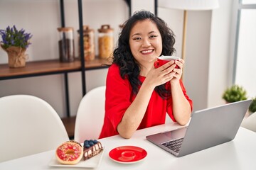 Canvas Print - Young chinese woman having breakfast using laptop at home