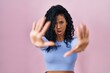 Middle age hispanic woman standing over pink background doing stop gesture with hands palms, angry and frustration expression