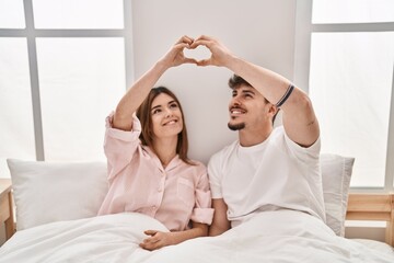 Wall Mural - Mand and woman couple doing heart gesture sitting on bed at bedroom