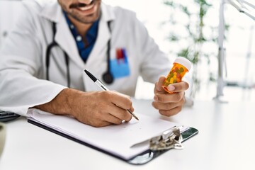 Wall Mural - Handsome hispanic man working as doctor writing pills presciption at hospital clinic