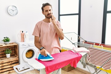 Canvas Print - Young hispanic man ironing clothes at home touching mouth with hand with painful expression because of toothache or dental illness on teeth. dentist concept.