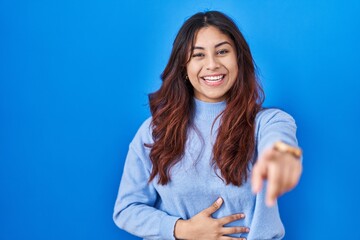 Canvas Print - Hispanic young woman standing over blue background laughing at you, pointing finger to the camera with hand over body, shame expression