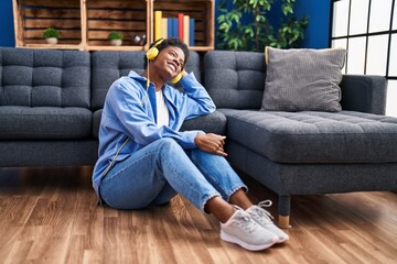 Wall Mural - African american woman listening to music sitting on floor at home