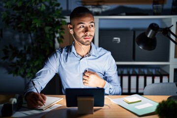 Poster - Young hispanic man working at the office at night smiling looking to the side and staring away thinking.