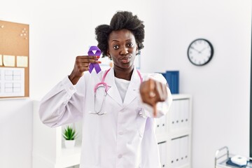 Poster - African doctor woman holding purple ribbon awareness at medical clinic pointing with finger to the camera and to you, confident gesture looking serious