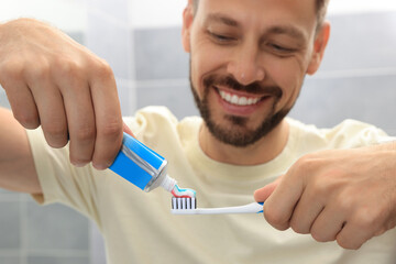 Wall Mural - Man applying toothpaste onto brush in bathroom, focus on hands