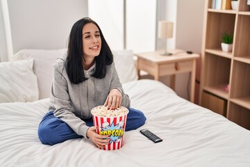 Sticker - Hispanic woman eating popcorn watching a movie on the bed winking looking at the camera with sexy expression, cheerful and happy face.