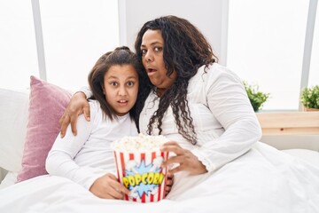 Sticker - Mother and young daughter eating popcorn in the bed in shock face, looking skeptical and sarcastic, surprised with open mouth