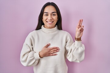 Poster - Young south asian woman standing over pink background smiling swearing with hand on chest and fingers up, making a loyalty promise oath