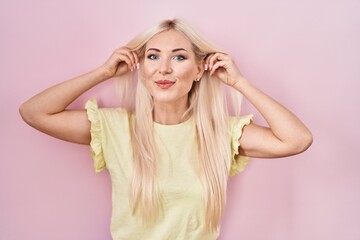 Sticker - Caucasian woman standing over pink background smiling pulling ears with fingers, funny gesture. audition problem