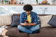 © kucherav - Young indian man playing video games using mobile phone. Asian male with curly hair holding smartphone communicate online in social networks sitting at home on the sofa