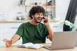 © kucherav - Happy young man freelancer or aspiring entrepreneur working remotely online at home office using laptop, talking on mobile phone, smiling friendly