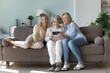 Elderly grandmother with mature daughter, young adult granddaughter spend time together watching online content, staring together on modern cellphone screen smile enjoy videos or new mobile apps. Tech