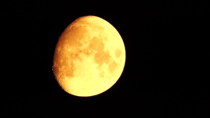 Wall Mural - A glowing golden huge moon seen from earth through the atmosphere against a starry night sky. A large moon moves across the sky, the moon moving from the left frame to the right.