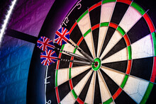Three Darts With Uk Flag Flights In Triple Double Bullseye On Professional Sisal Steeldart Board In Colorful LED Illumination On White Stone Wall. Perfect Shot Hobby Sport Concept  Background.