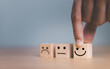 © Suriya - Close up customer hand choose smile face and blurred sad face icon on wood cube, Service rating, Customer service evaluation and satisfaction survey concepts.