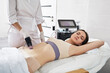 Woman during RF lifting procedure for her body skin tightening with cosmetologist at beauty salon. RF body lifting