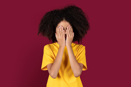 Frightened girl looking covering face isolated on burgundy studio background
