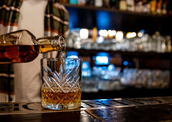 Wall Mural - Bartender pouring whiskey from bottle on glass in bar