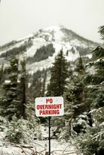 Selective Focus On A No Overnight Parking Sign With Snowy Trees And A Mountain In The Background