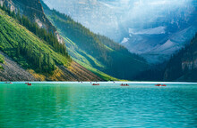 Lake Louise With Canoes In The Afternoon Of A Summer Day. Green Water And Sun Setting Behind The Mountains.