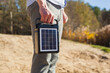 A guy carries a portable solar panel for charging equipment. The model is holding a portable battery for nature.
