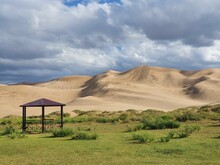 Breathtaking View Of An Green Field With A Gazebo In The Middle Of Sandy Desert With A Sandy Dune
