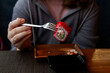 the hands of a teenager in a gray hoodie are holding sushi food with a European device with an iron fork, a girl in gray-colored cafe clothes is eating Japanese food