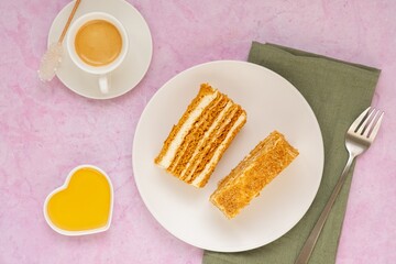 Wall Mural - Dessert, sliced layered honey cake with cream on a white plate on a pink concrete background. Valentine's day concept.