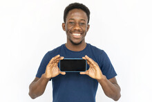 Cheerful Man Showing Phone Screen. Young African American Male Model In Blue T-shirt Holding Smartphone Horizontally, Presenting App. Portrait, Studio Shot, Technology, Advertising Concept