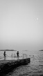 Vertical grayscale of kids playing on the dock by a sea and getting ready to jump into the water