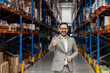 A businessman is giving thumbs up while smiling at the camera in warehouse.