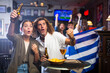 © JackF - Happy multiracial soccer fans with flag of Greece celebrating victory of team with pint of beer and chips in the pub