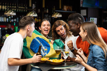 Multiracial Brazil Sports Fans, Men And Women, Supporting Their Favourite Team In Bar, Raising State Flag And Screaming Chants Together.