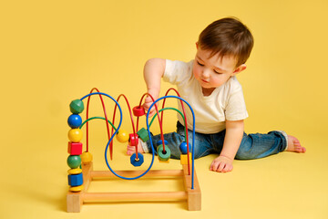 Wall Mural - Toddler baby is playing logic educational games on a studio yellow background. Happy child play with educational toy, learning logic. Kid aged one year four months