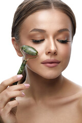 Wall Mural - Beauty skin care. Woman using jade facial roller for face massage. Girl using natural massager for spa treatment.