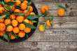 Mandarin oranges with leaves on black tray on  wooden background. Pile of fresh tangerine fruits on wooden table. Top view. Copy space.