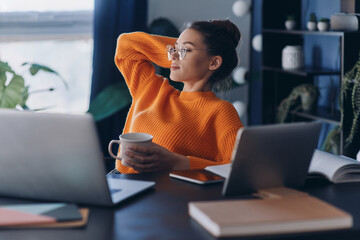 Relaxed woman holding her feet on desk and enjoying coffee while sitting at her working place in office