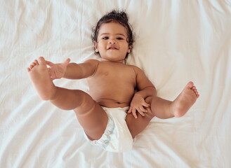 happy, smile and portrait of a baby with a diaper relaxing on a bed in his bedroom or nursery. happi